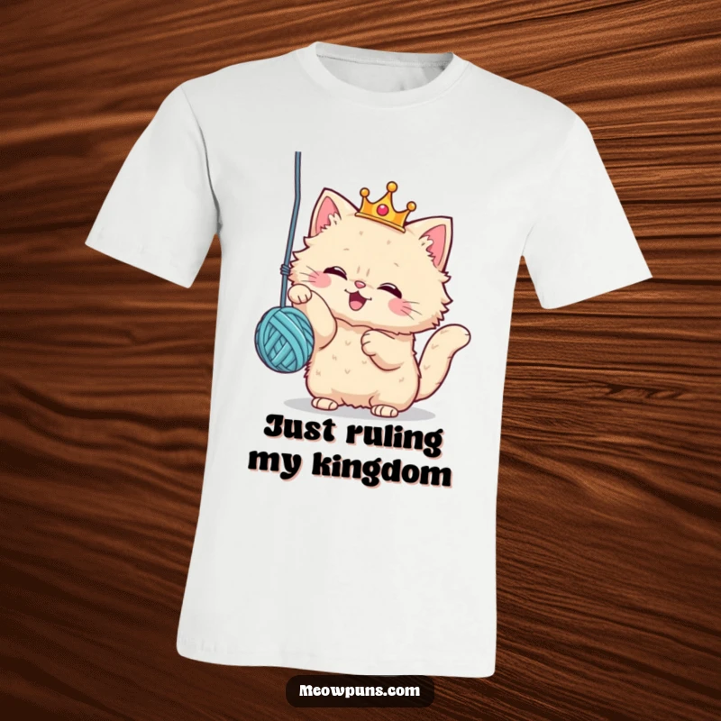 Funny cat t-shirt featuring a fluffy cat wearing a tiny crown, enthusiastically swatting at a dangling yarn ball, embodying regal playfulness.